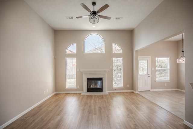 unfurnished living room with light wood-type flooring, visible vents, and a glass covered fireplace