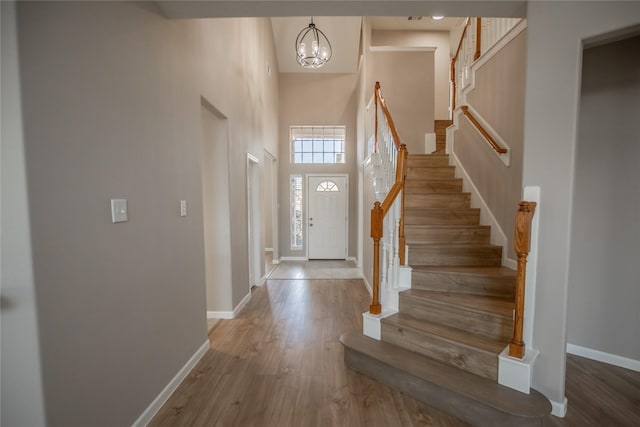 foyer with baseboards, stairs, a high ceiling, an inviting chandelier, and wood finished floors