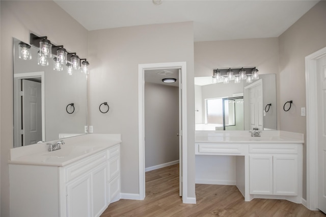 full bath featuring two vanities, wood finished floors, baseboards, and a sink