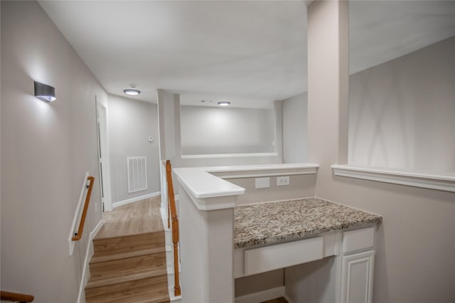 interior space featuring light stone counters, wood finished floors, visible vents, baseboards, and built in desk