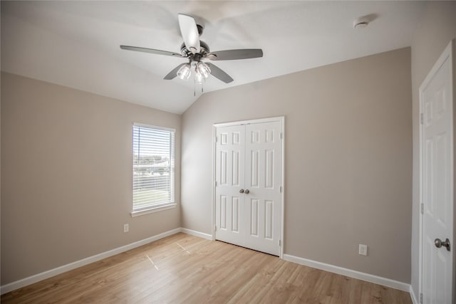 unfurnished bedroom featuring a ceiling fan, baseboards, light wood-style flooring, vaulted ceiling, and a closet