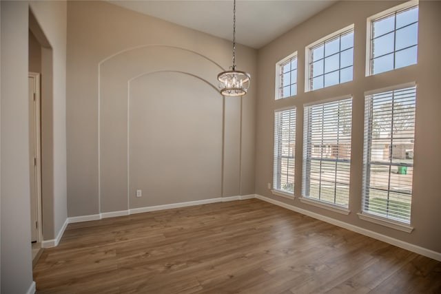 spare room featuring a notable chandelier, a healthy amount of sunlight, baseboards, and wood finished floors