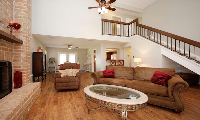 living area featuring a brick fireplace, stairs, ceiling fan, and wood finished floors