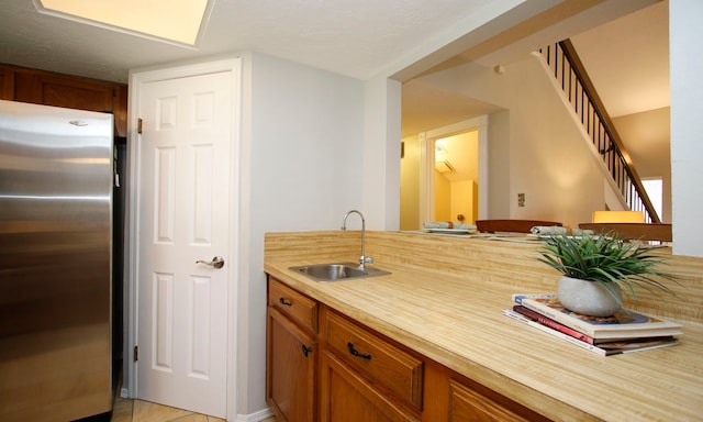 kitchen with light countertops, brown cabinetry, freestanding refrigerator, and a sink