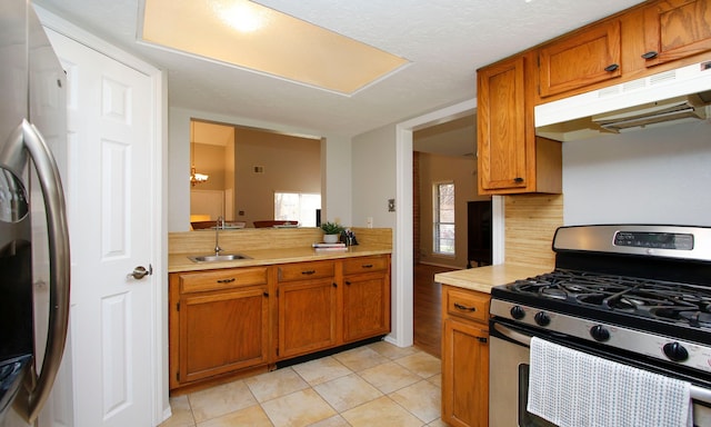 kitchen featuring under cabinet range hood, light countertops, brown cabinetry, stainless steel appliances, and a sink