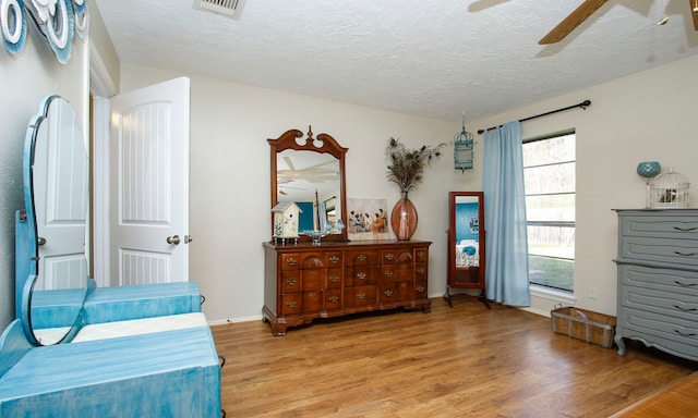 bedroom featuring visible vents, baseboards, ceiling fan, wood finished floors, and a textured ceiling