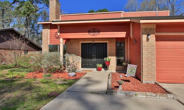 doorway to property featuring a garage, brick siding, and a chimney