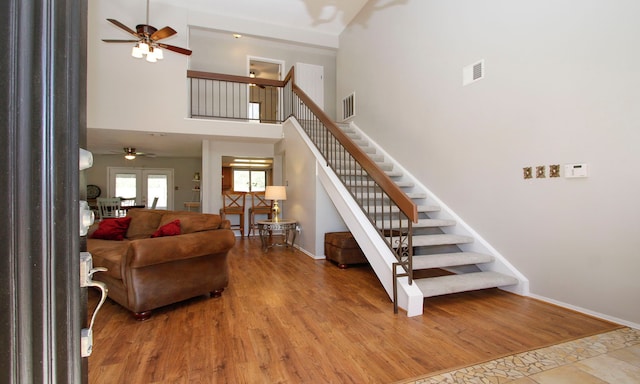 staircase with visible vents, baseboards, a high ceiling, and wood finished floors