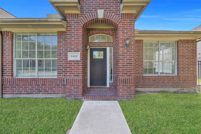 view of exterior entry featuring a yard and brick siding