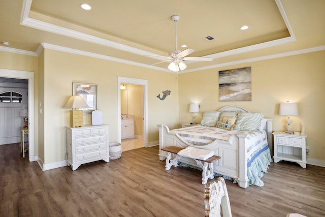 bedroom featuring visible vents, crown molding, baseboards, wood finished floors, and a raised ceiling