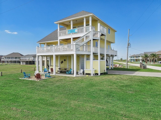 back of property featuring a fire pit, a lawn, roof with shingles, and a patio area