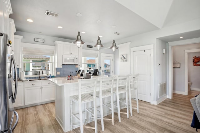 kitchen with visible vents, white cabinets, white microwave, and stainless steel refrigerator with ice dispenser