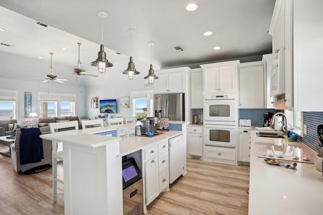 kitchen featuring open floor plan, white appliances, white cabinets, light countertops, and decorative backsplash