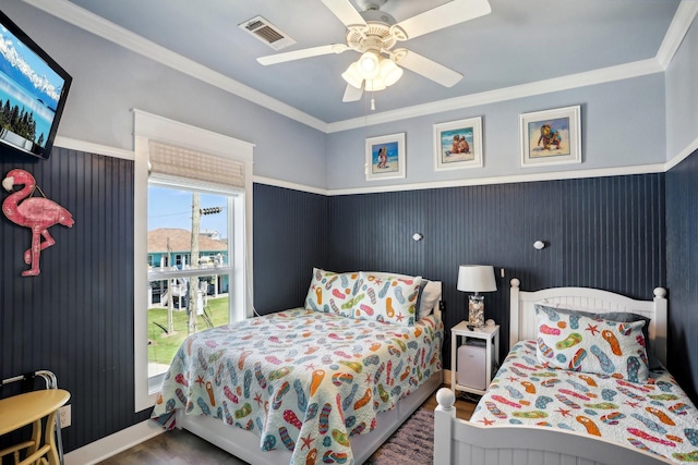 bedroom with visible vents, crown molding, ceiling fan, wainscoting, and wood finished floors