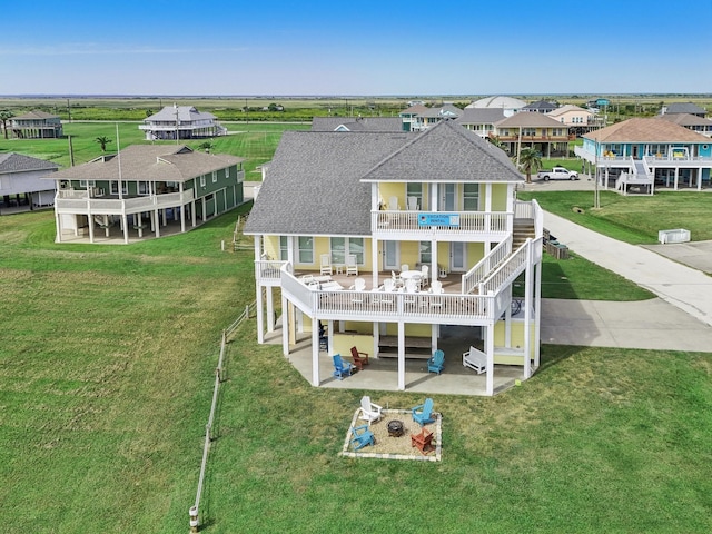 rear view of house featuring a lawn, a residential view, a shingled roof, a balcony, and a patio area