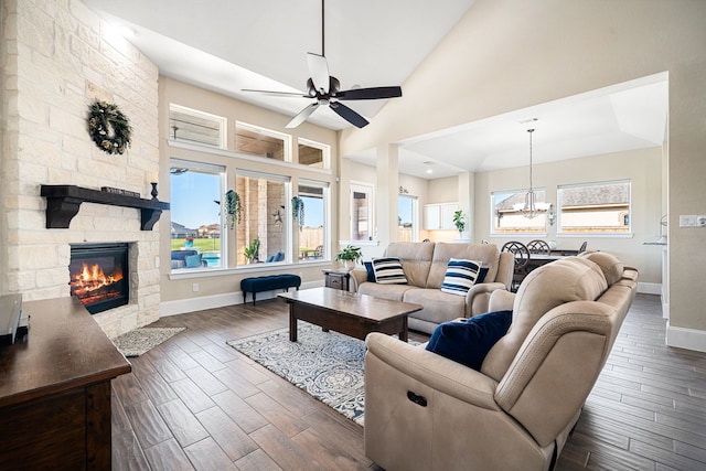 living room with a fireplace, ceiling fan with notable chandelier, dark wood-style floors, and baseboards