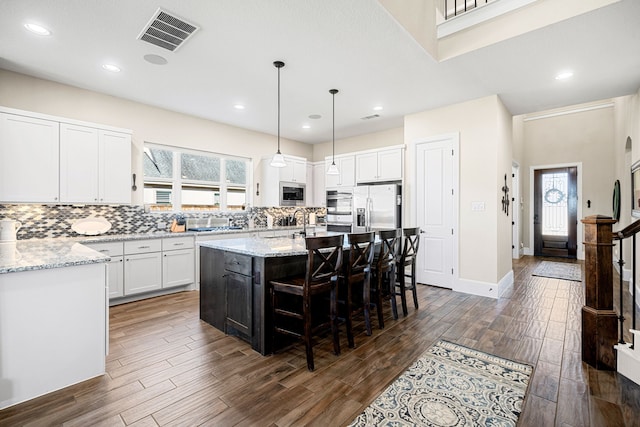 kitchen with tasteful backsplash, visible vents, light stone counters, white cabinets, and stainless steel appliances