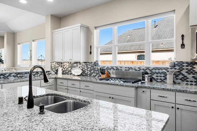 kitchen with light stone countertops, stainless steel gas cooktop, decorative backsplash, recessed lighting, and a sink