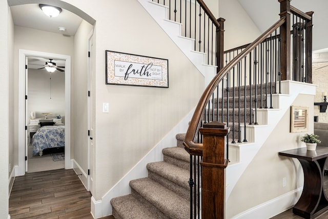 staircase featuring baseboards, wood finished floors, arched walkways, and ceiling fan