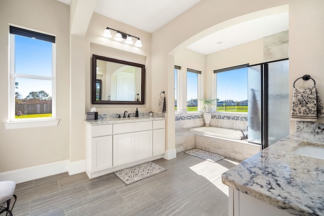 bathroom with baseboards, two vanities, a stall shower, a bath, and a sink