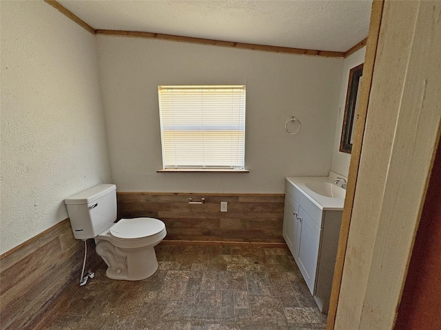 bathroom featuring a wainscoted wall, toilet, a textured ceiling, wood walls, and vanity