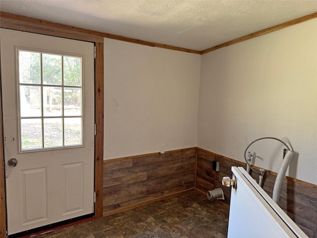 doorway featuring a wealth of natural light, a textured ceiling, wood walls, and wainscoting