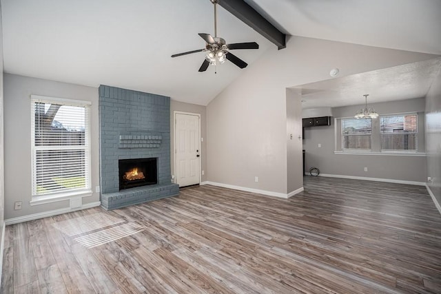 unfurnished living room with wood finished floors, baseboards, a fireplace, beamed ceiling, and ceiling fan with notable chandelier