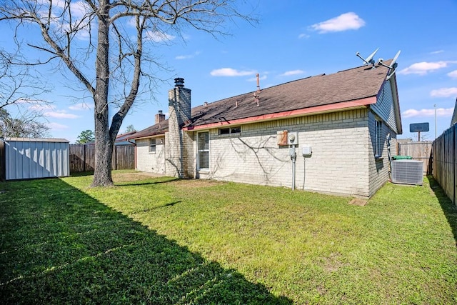 rear view of property with brick siding, a chimney, a fenced backyard, an outbuilding, and a storage unit