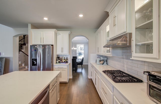 kitchen with under cabinet range hood, appliances with stainless steel finishes, white cabinetry, and arched walkways