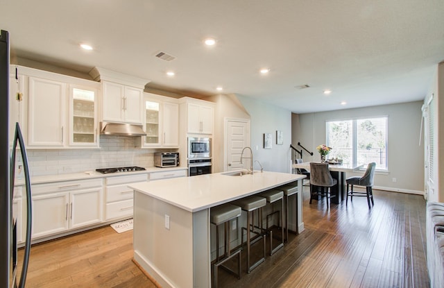 kitchen featuring visible vents, stainless steel appliances, a sink, under cabinet range hood, and backsplash