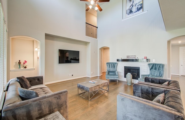 living room with wood finished floors, baseboards, arched walkways, ceiling fan, and a glass covered fireplace