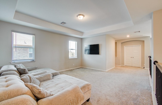 living area with a tray ceiling, baseboards, light colored carpet, and visible vents