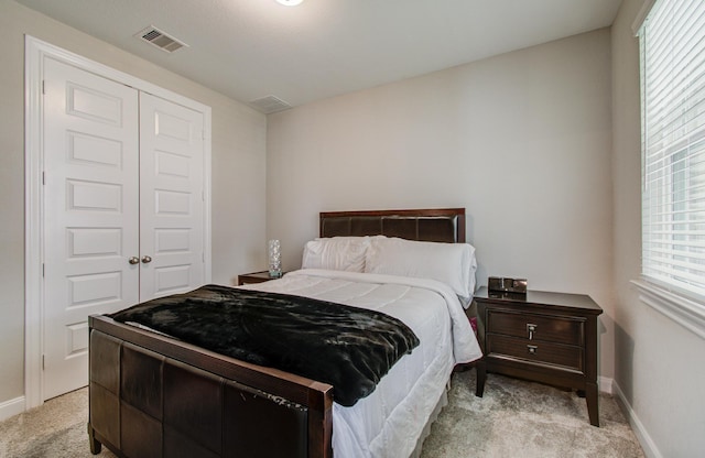 bedroom with baseboards, visible vents, a closet, and light carpet