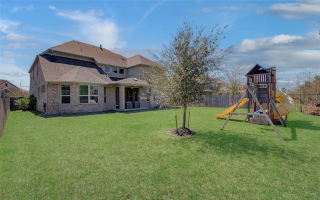 back of property with brick siding, a shingled roof, a playground, a fenced backyard, and a yard