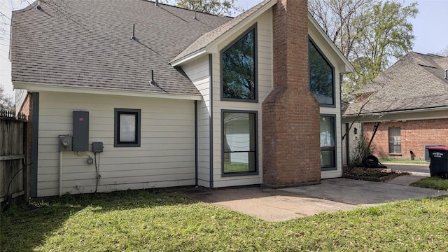 back of property featuring fence, roof with shingles, a chimney, a patio area, and a lawn