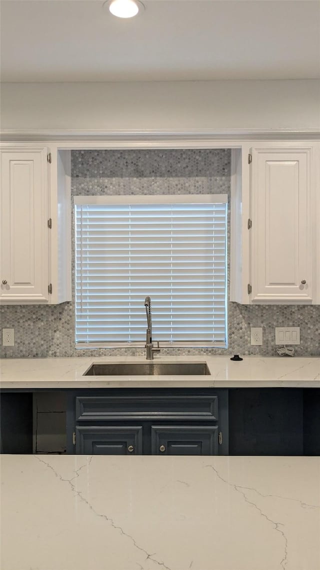 kitchen featuring a sink, light stone countertops, backsplash, and white cabinets