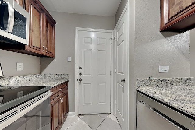 kitchen featuring light tile patterned floors, stainless steel appliances, baseboards, and light stone countertops