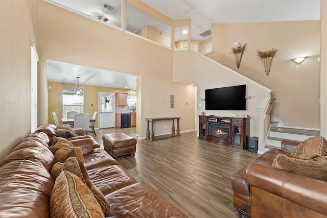 living room featuring a towering ceiling, wood finished floors, visible vents, and a warm lit fireplace