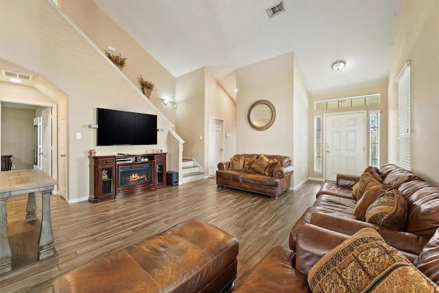 living area featuring visible vents, high vaulted ceiling, baseboards, and wood finished floors