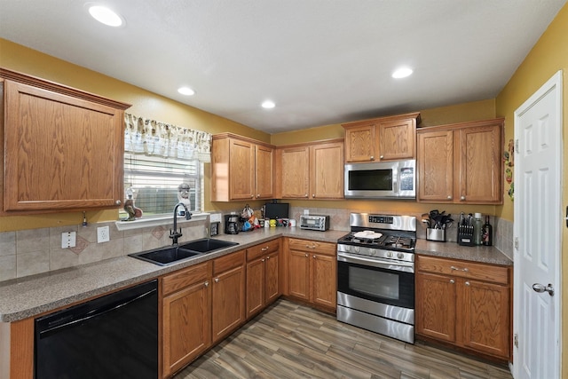 kitchen with wood finished floors, recessed lighting, a sink, decorative backsplash, and appliances with stainless steel finishes