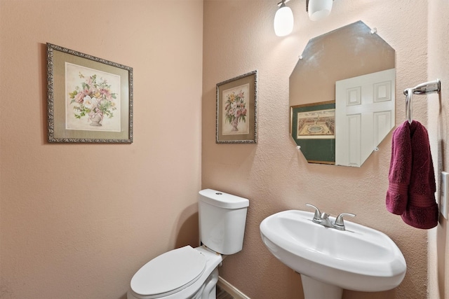 bathroom with toilet, a textured wall, and a sink