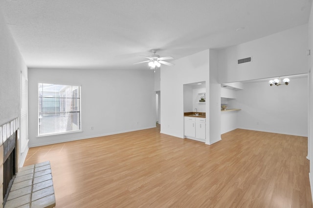 unfurnished living room with light wood finished floors, visible vents, ceiling fan with notable chandelier, and a fireplace