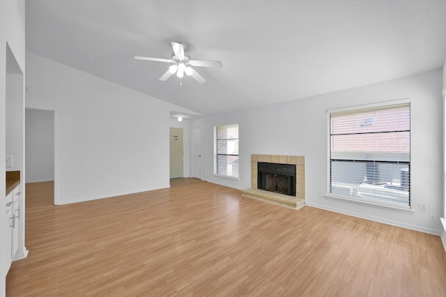 unfurnished living room featuring baseboards, light wood-style flooring, a tile fireplace, ceiling fan, and vaulted ceiling