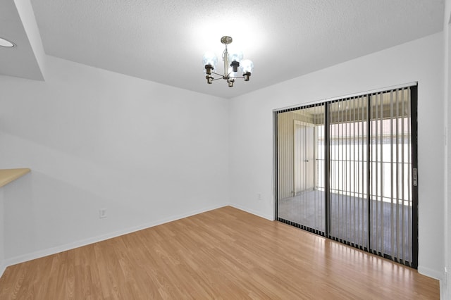 empty room with baseboards, a notable chandelier, wood finished floors, and a textured ceiling