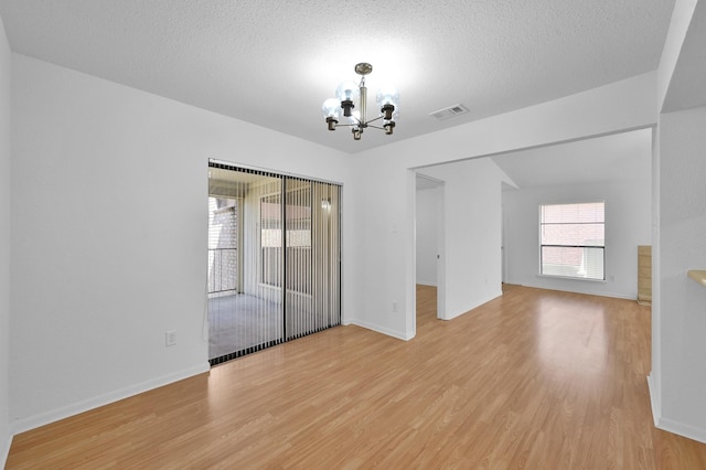 empty room with an inviting chandelier, visible vents, light wood-type flooring, and a textured ceiling