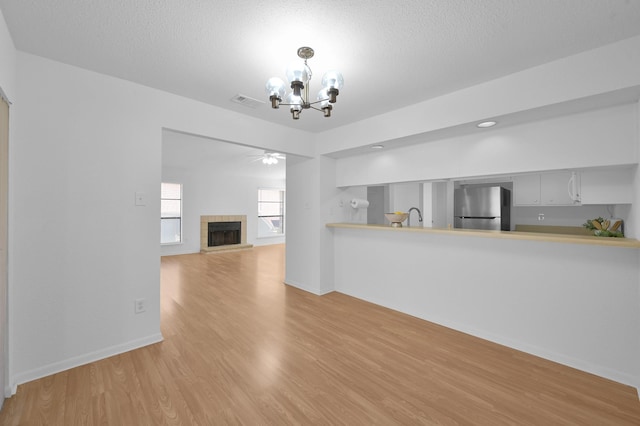 unfurnished living room featuring light wood finished floors, a sink, a textured ceiling, a tiled fireplace, and ceiling fan with notable chandelier