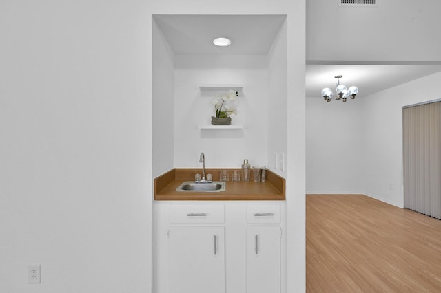 bar featuring visible vents, wet bar, an inviting chandelier, a sink, and light wood-type flooring