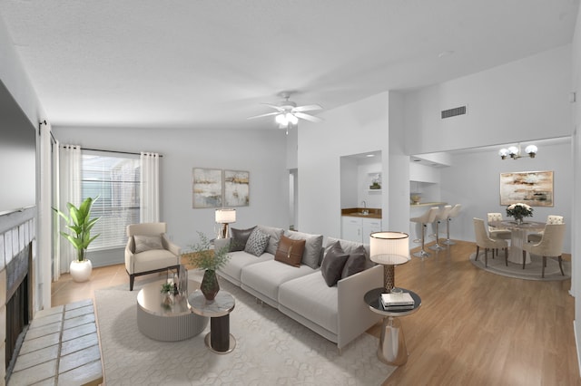 living room with visible vents, light wood finished floors, a fireplace, ceiling fan, and vaulted ceiling