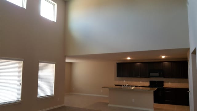 kitchen featuring baseboards, an island with sink, a towering ceiling, black appliances, and a sink