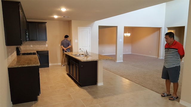 kitchen with light stone counters, an island with sink, a sink, light colored carpet, and tasteful backsplash